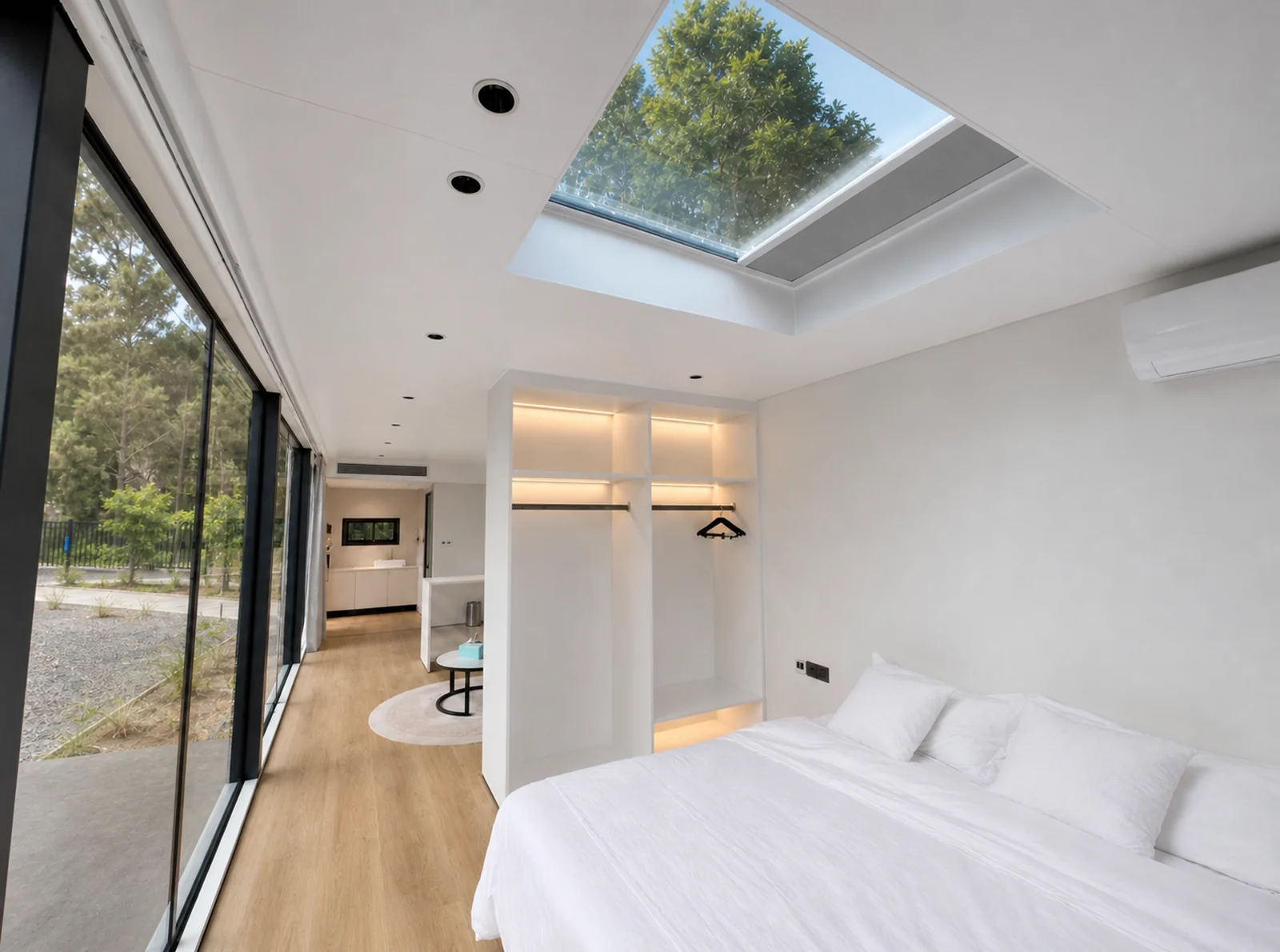 Bedroom end of the capsule, double bed against a lit open wardrobe, glass skylight overhead and full height glazing looking out to trees