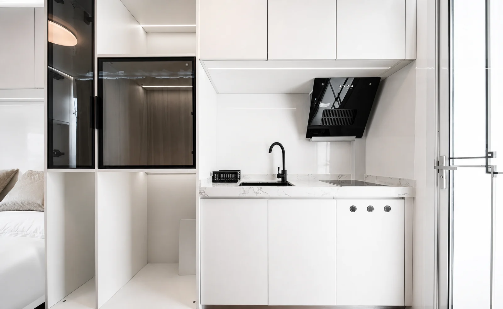 Kitchen end of the 5.8 m home, white gloss cabinets with a rangehood, black tapware and an induction cooktop, with the bed just past the partition