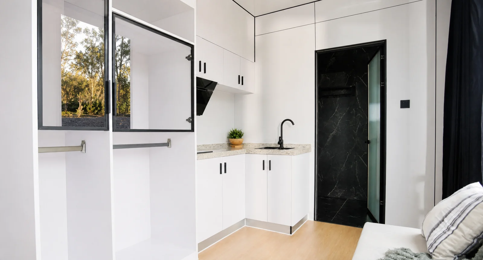 Corner kitchen inside the 8.5 m home, white cabinets with a speckled bench, black tapware and rangehood, with a black marble look bathroom door alongside