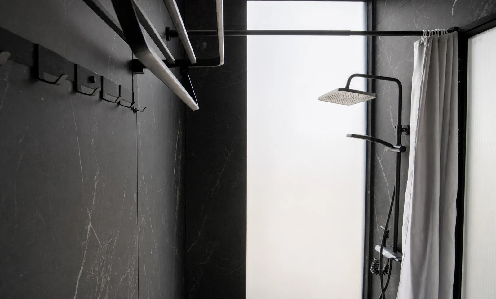 Bathroom in the 8.5 m home, black marble look wall with a square rain shower head and hand shower behind the curtain, robe hooks on the wall