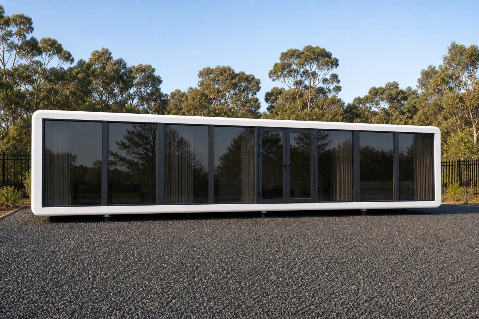 Long white MD115D module with continuous dark glazing and drawn curtains running the full length, on a gravel pad at dusk