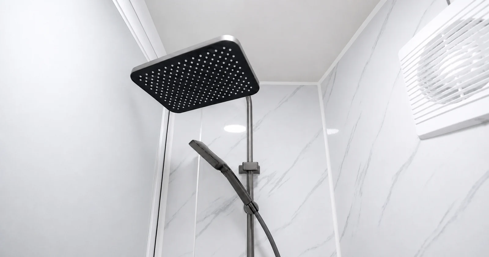 Shower in the studio bathroom, large square rain head and hand shower on a white marble look wall with a ceiling exhaust vent