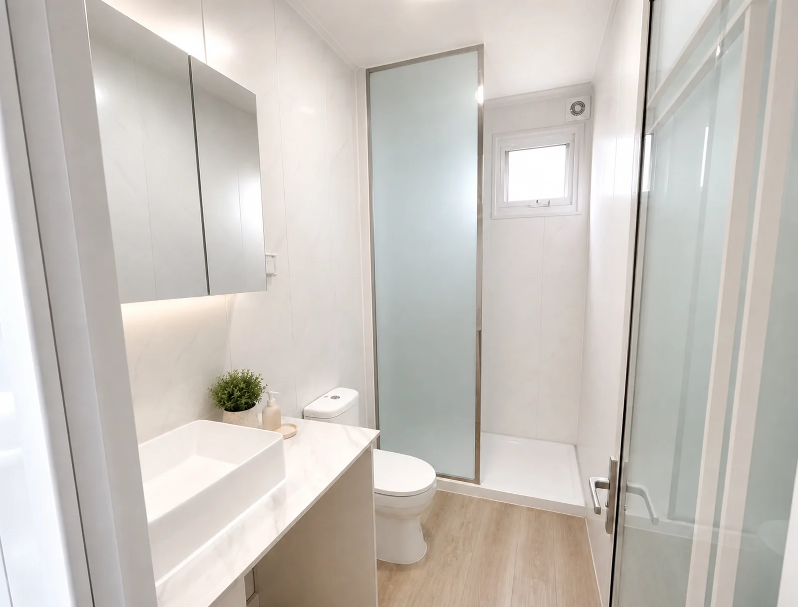Bathroom in the 9 m home, wall hung basin with mirrored cabinets above, toilet alongside and a glass screened shower with a small window