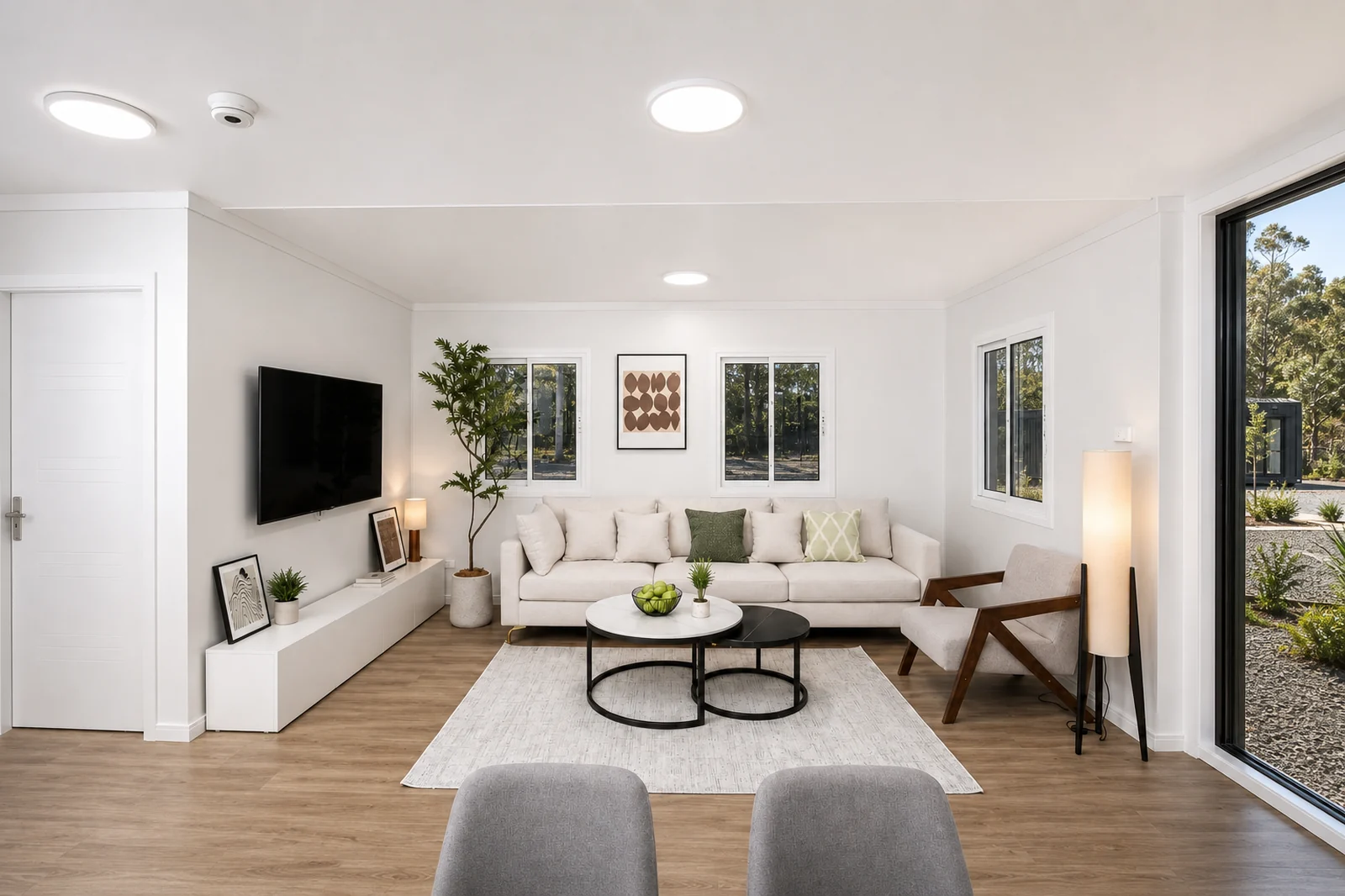 Living room of the 11.8 m home, corner sofa and coffee table on a pale rug with a wall mounted television and sliding doors to the deck
