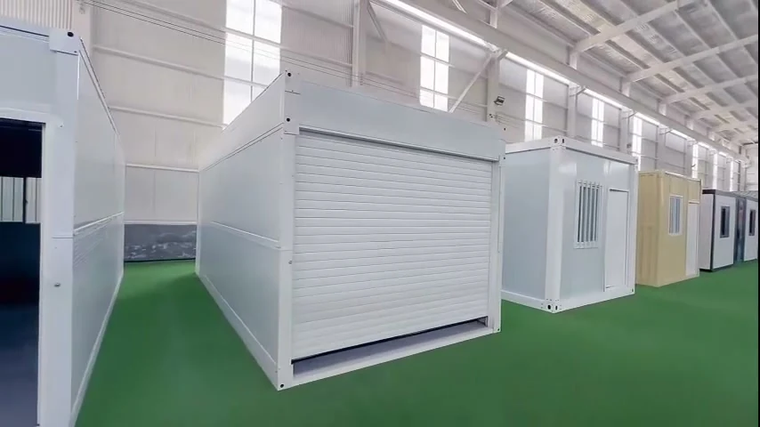 White folding garage standing on a factory floor with its roller door down, other flat pack cabins lined up behind it