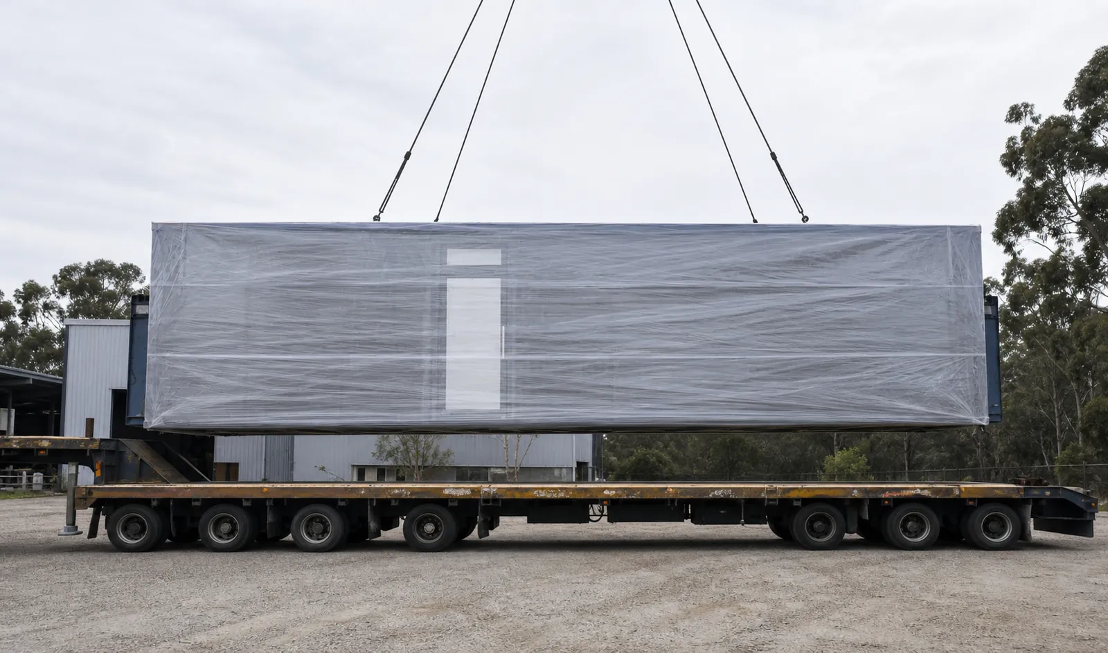 The 11.5 m mirror house wrapped in protective sheeting, slung from crane straps above a multi axle trailer ready for transport