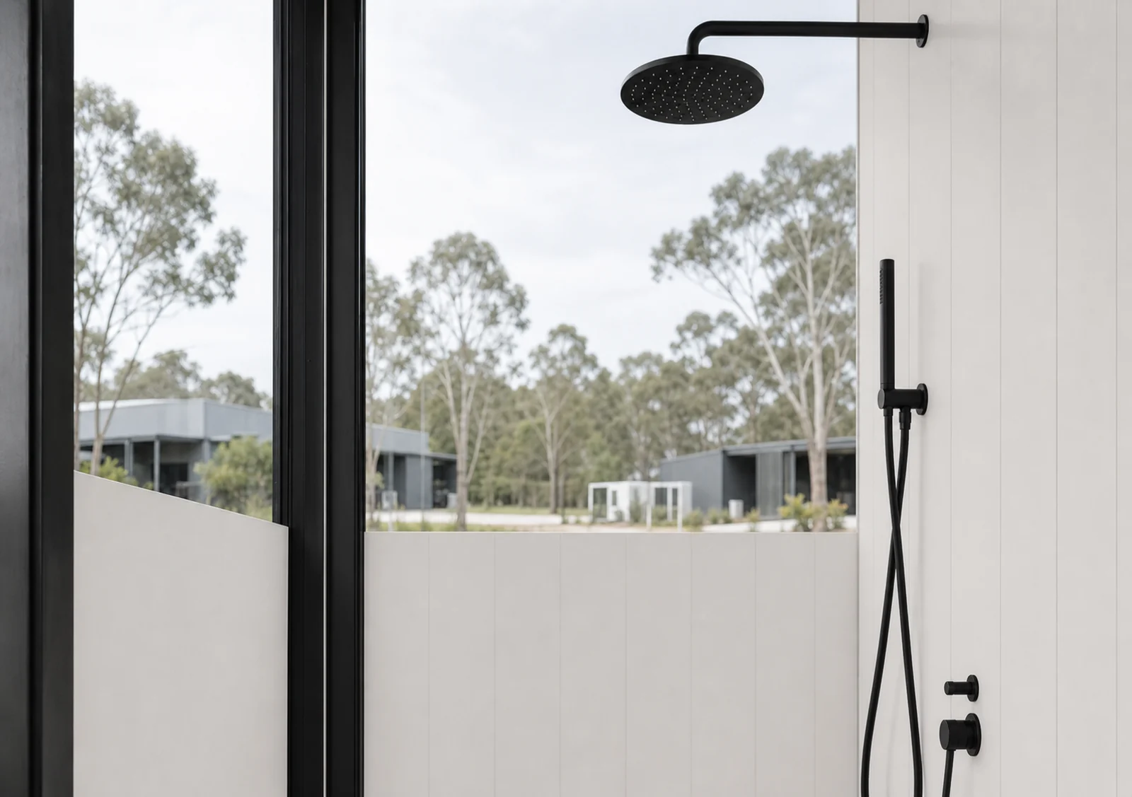 Shower in the wide mirror house, matte black rain head and hand shower on a white lined wall beside a full height window looking to the bush