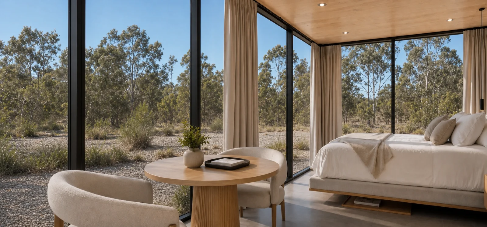Bedroom in the 8 m mirror house, round timber table and two boucle chairs by the glazed corner with the bed against a timber lined wall