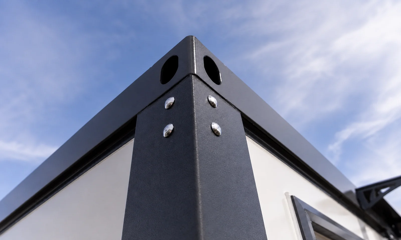 Close view of the cabin roof corner from below, the folded steel capping bolted to the corner post with two drain holes