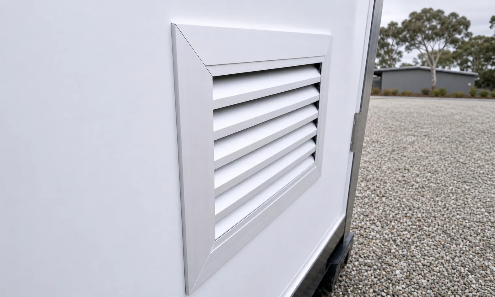 Close view of the louvred ventilation grille set into the white wall panel of the toilet cabin