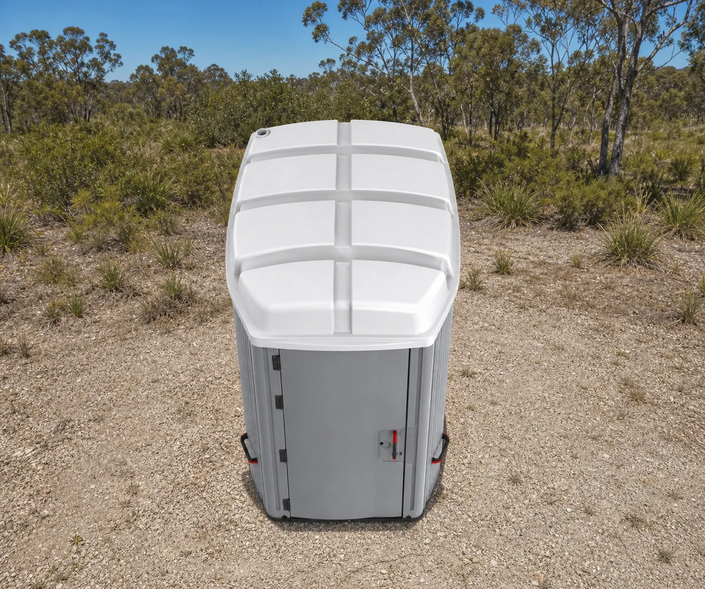 The accessible portaloo from behind on scrubby ground, ribbed grey panels and the white moulded roof, with tie down latches down the corner
