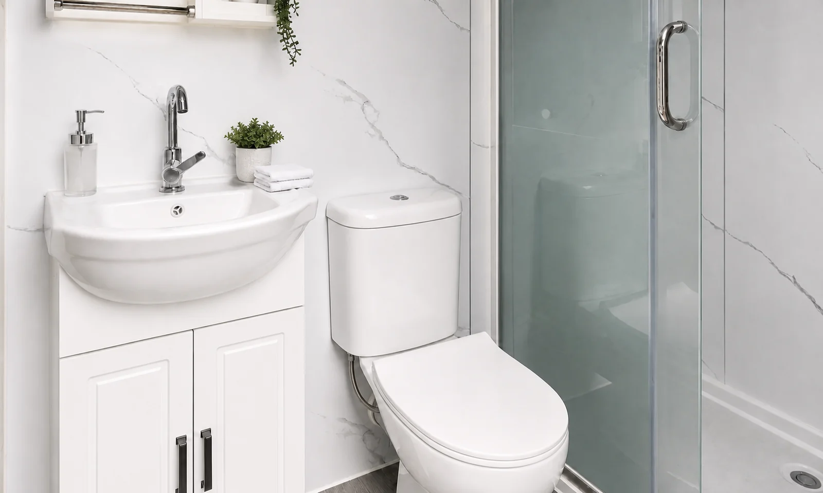 Inside a portable bathroom unit, with a white vanity and basin, a toilet and a glass shower screen against marble look wall panels