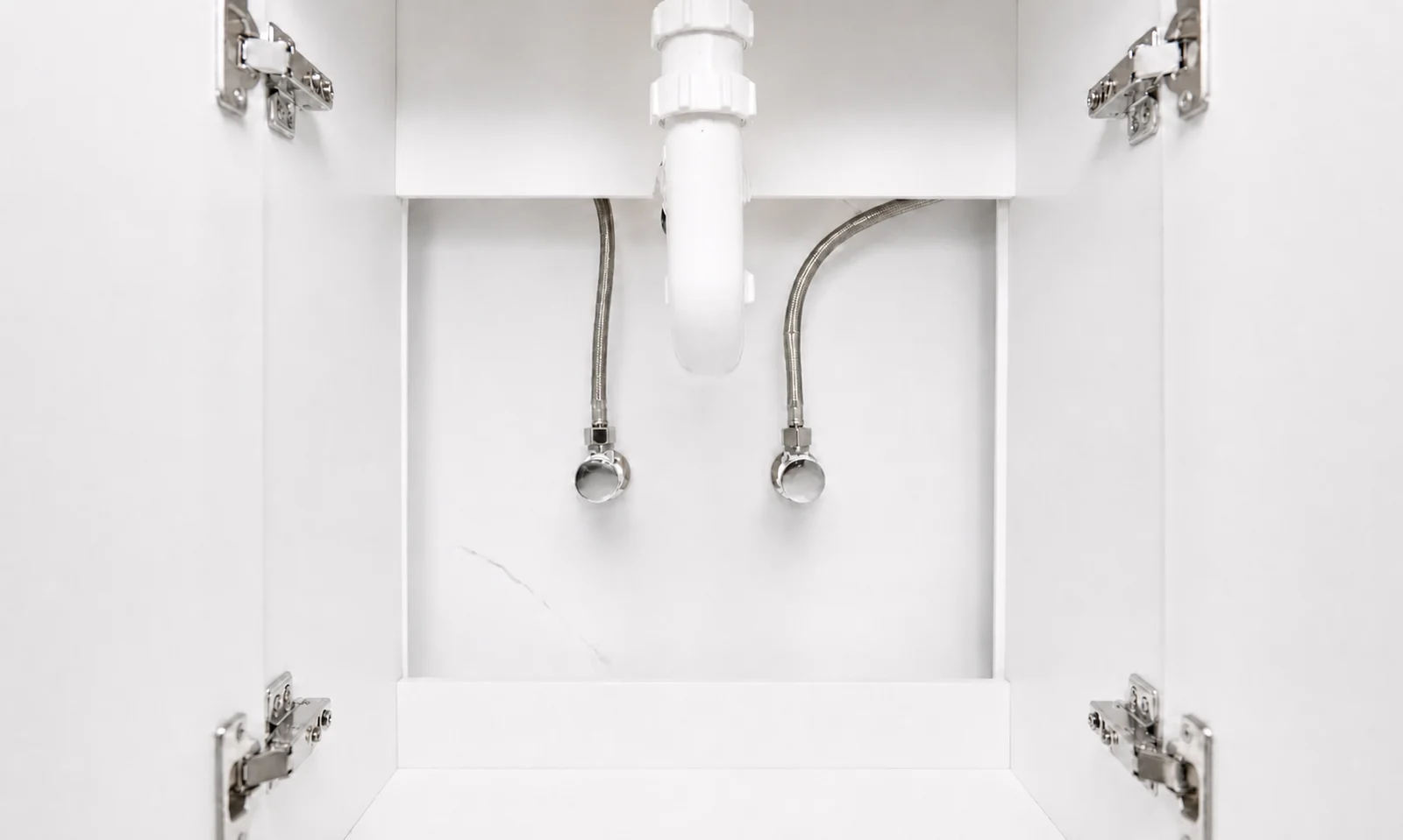 Inside the vanity cupboard of the portable bathroom, the basin trap and braided hot and cold flexible hoses