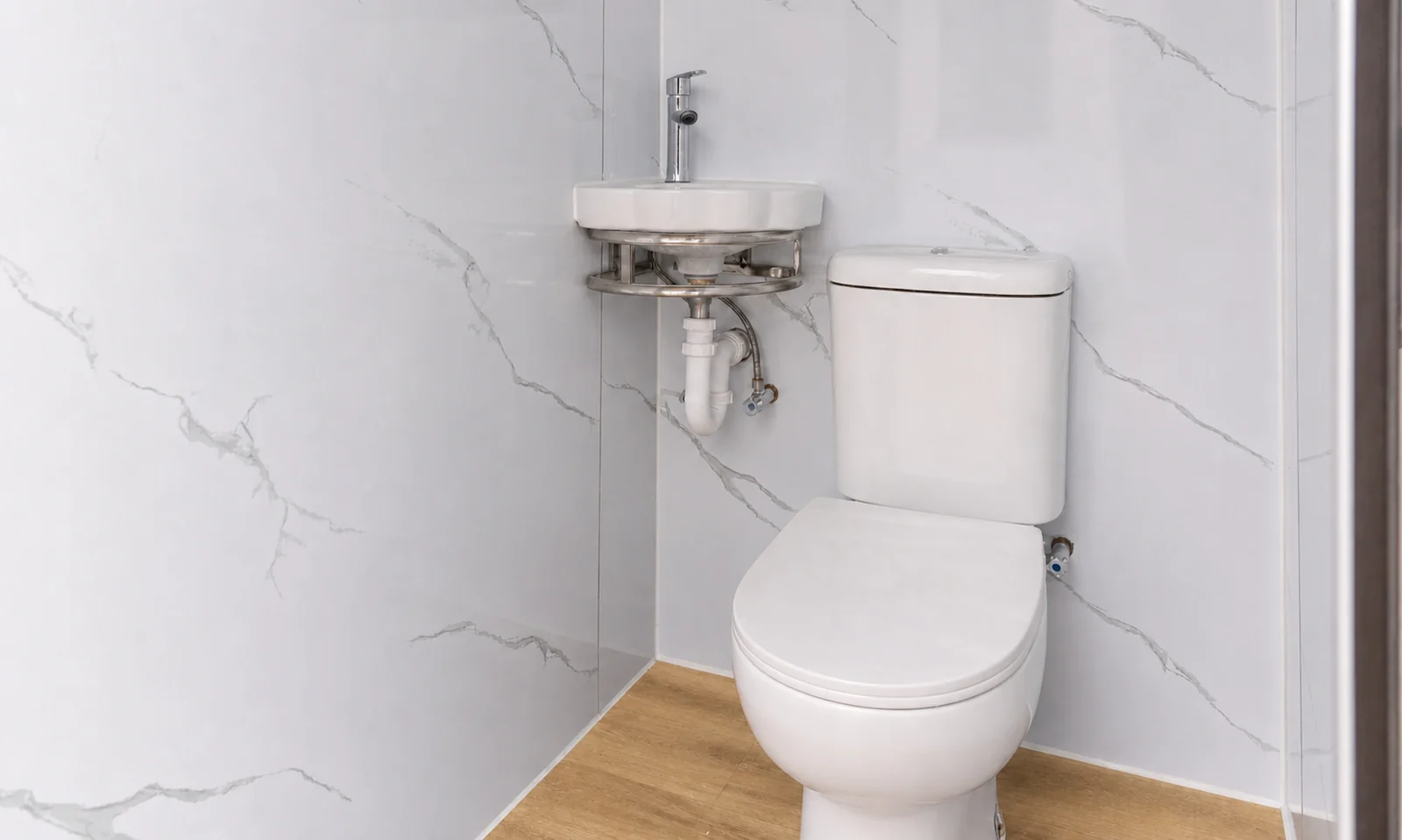 Inside one cubicle of the twin block, corner basin with a mixer above a close coupled toilet against marble look wall panels