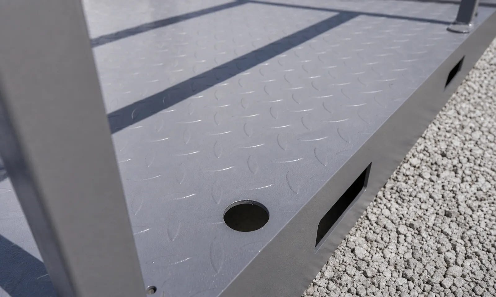 Close view of the chequer plate ramp deck and its folded steel edge where it meets the gravel