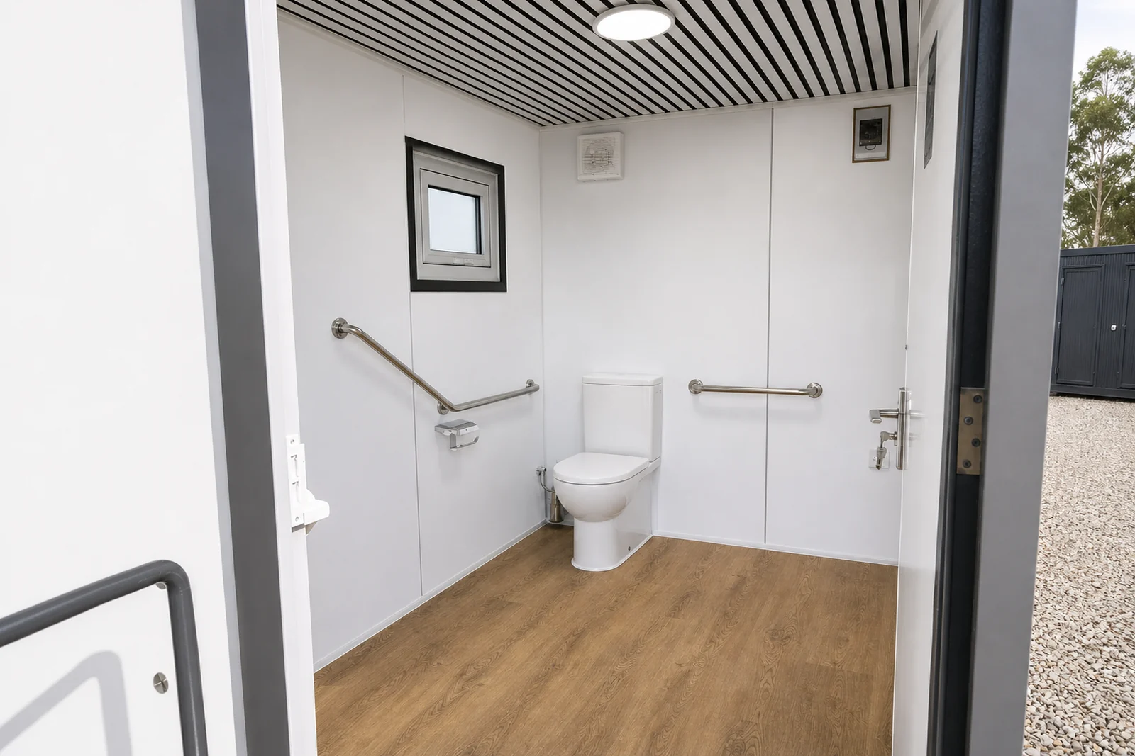 The accessible toilet from the doorway, grab rails either side of the toilet, a window above and a slatted ceiling with a round light