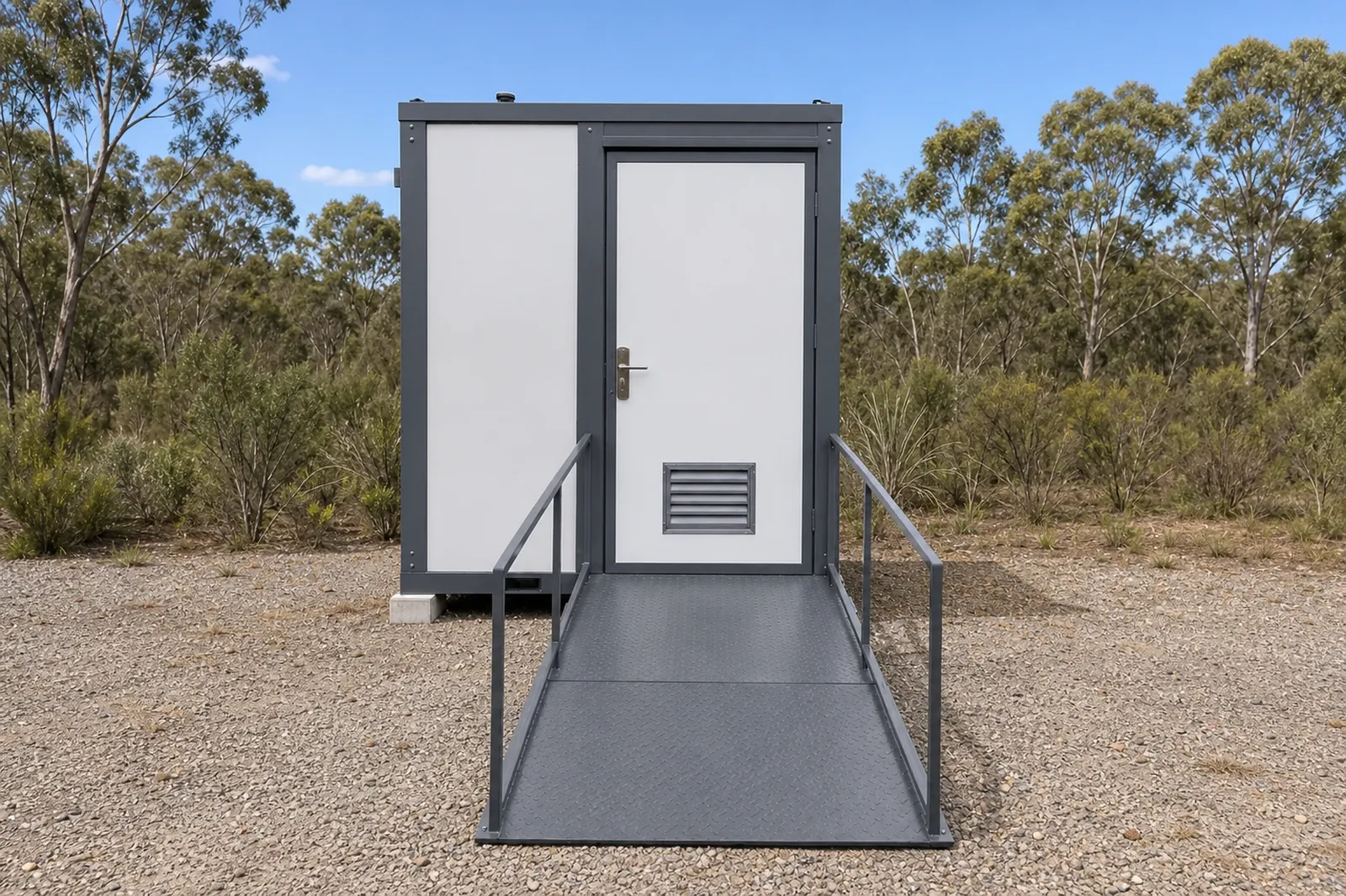 The accessible wet room cabin square on, white door with a floor vent at the top of the ramp, handrails either side, bush behind