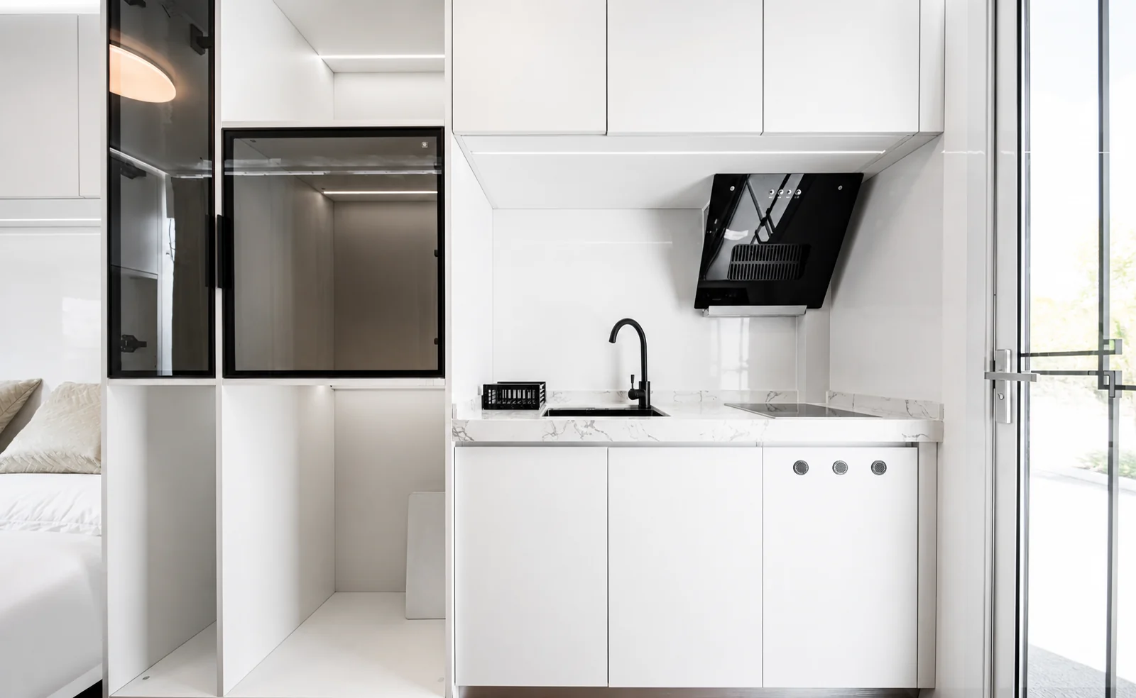 Two views inside the rounded capsule, an open storage wall and the bed on the left, the kitchen with a marble look benchtop on the right