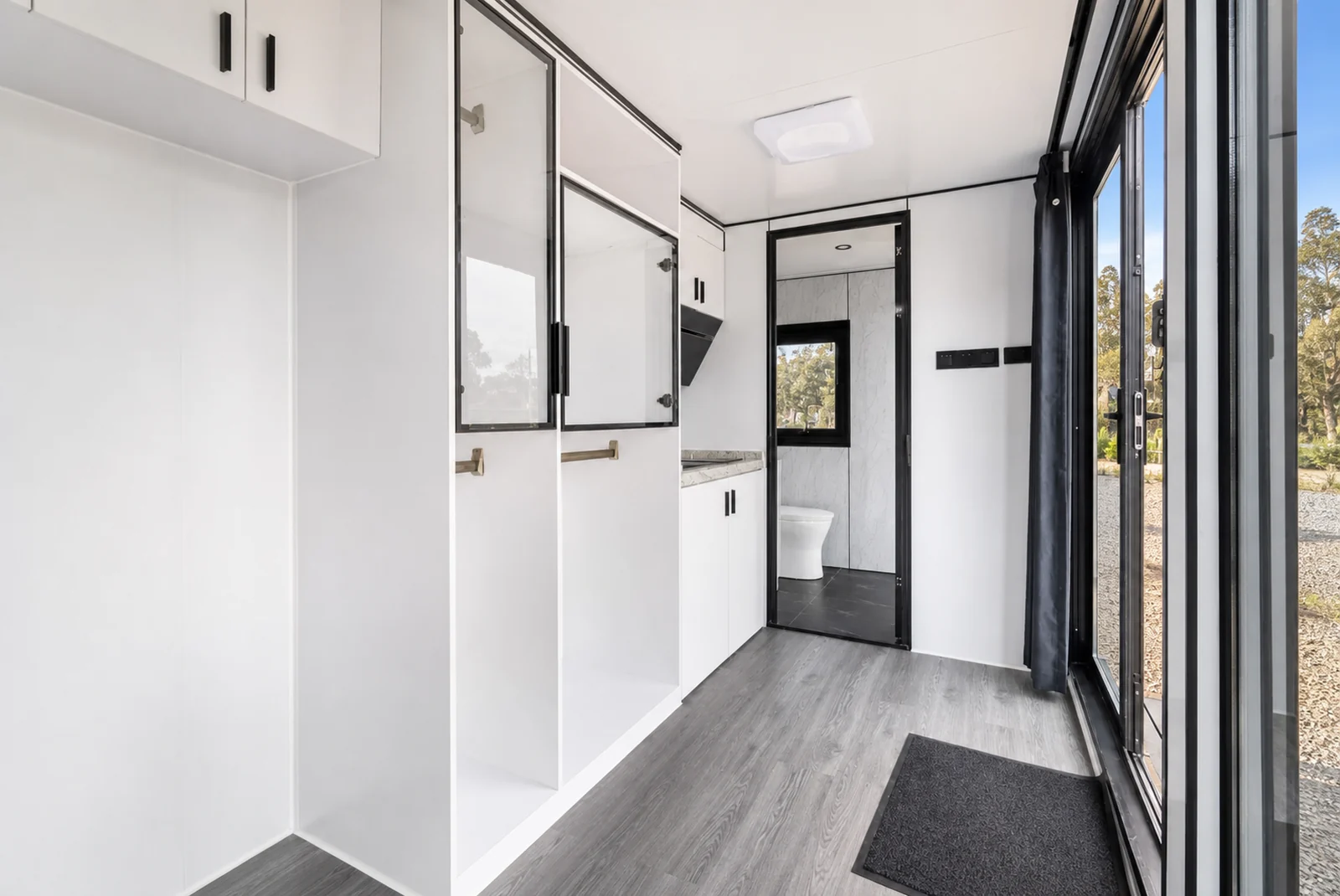 Looking down the rounded capsule from the entry, a tall storage cupboard on the left, the bathroom door ahead and glazing along the right