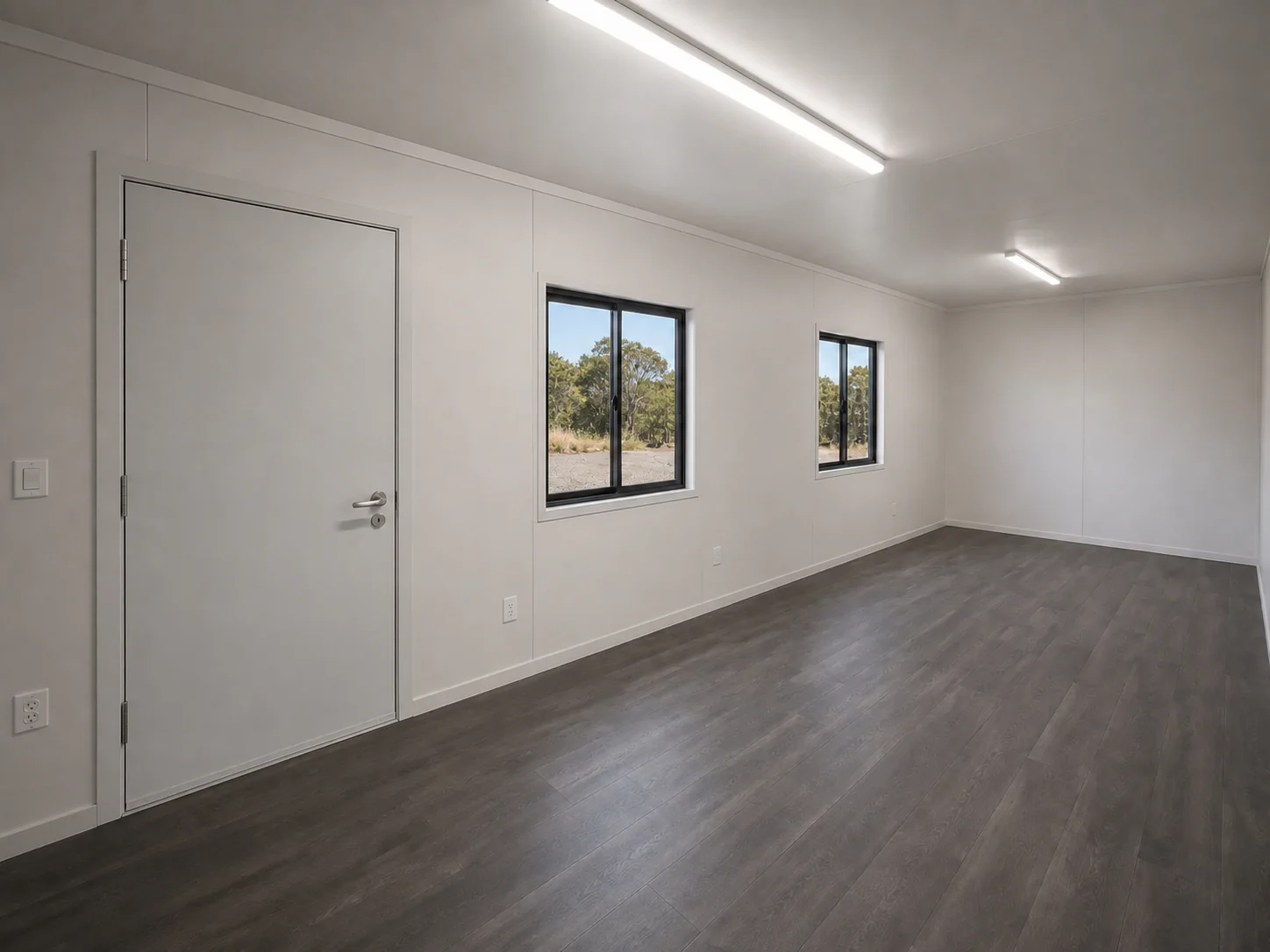Inside the 40ft office, an empty white lined room with dark timber look vinyl flooring, LED batten lights and two windows