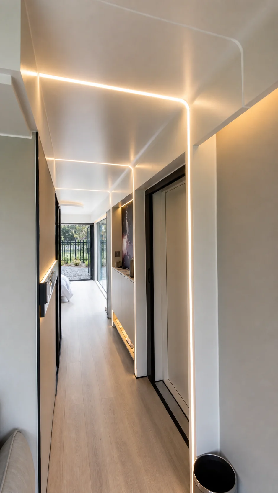 Corridor inside the capsule studio with concealed strip lighting running along the ceiling and a bathroom door in the side wall