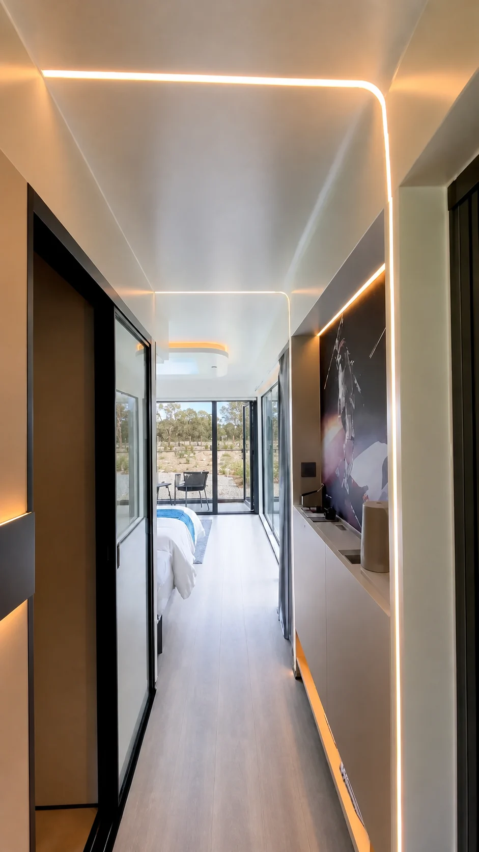 Looking along the capsule studio corridor to the bed at the far end, mirrored wardrobe doors on one side and glazing on the other