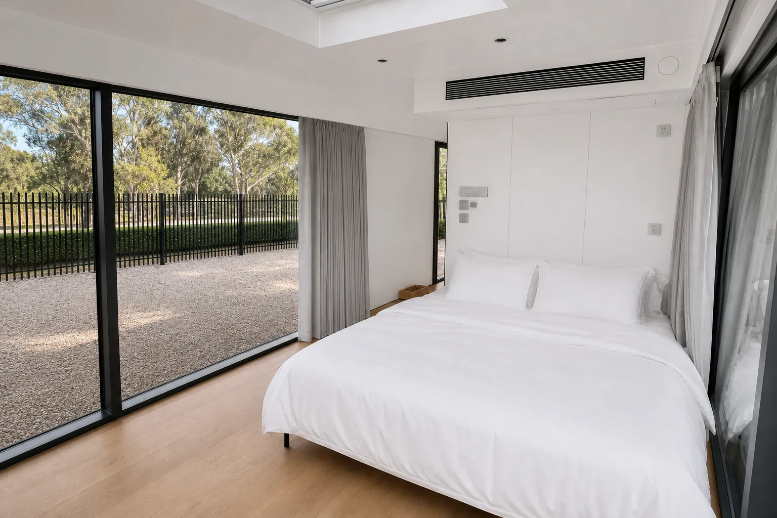 Bedroom in the balcony capsule, made double bed beside a full height glazed wall with curtains and a ceiling air outlet above