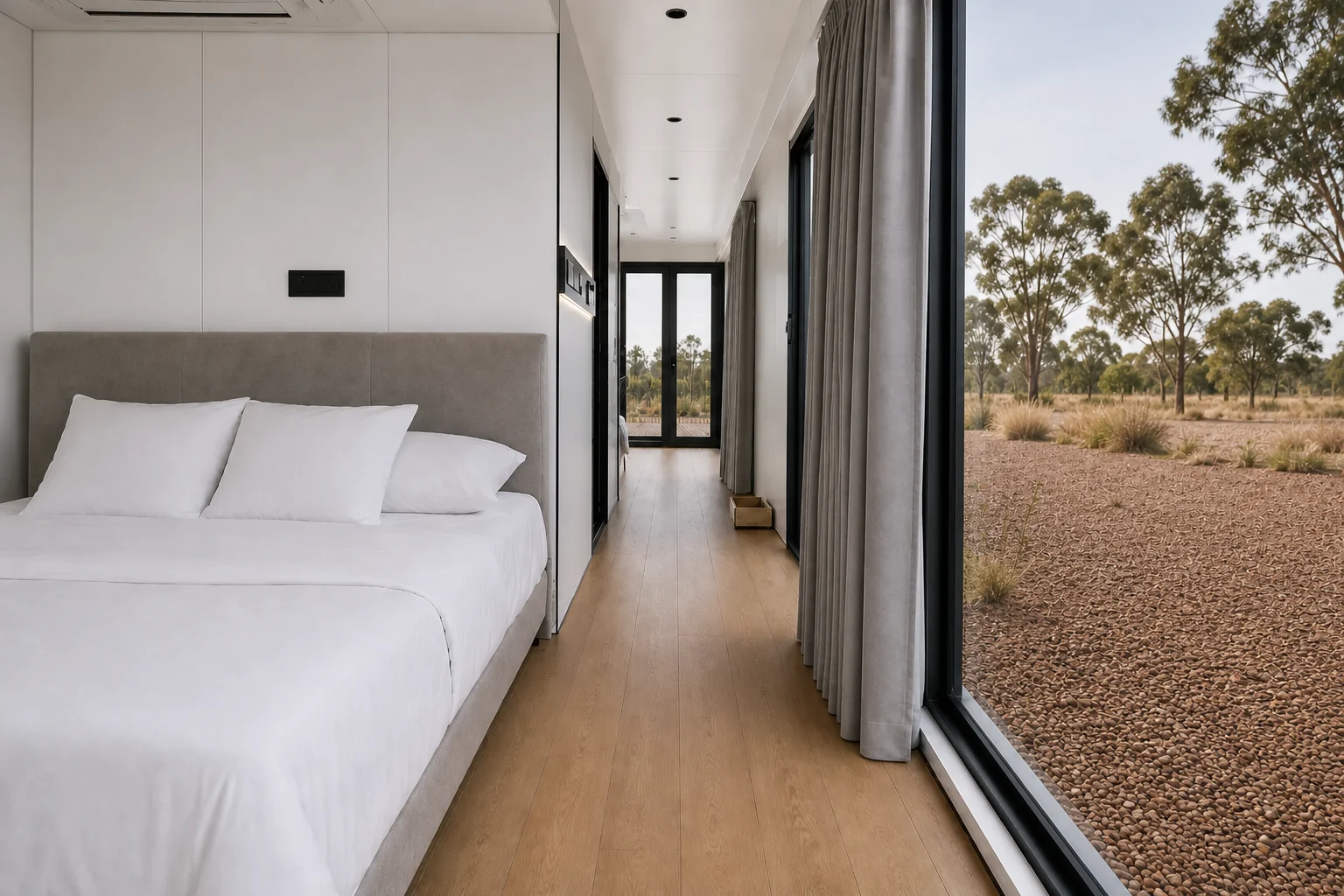 Double bed with an upholstered bedhead in the balcony capsule, curtains drawn back from the glazing to a gravel and scrub outlook