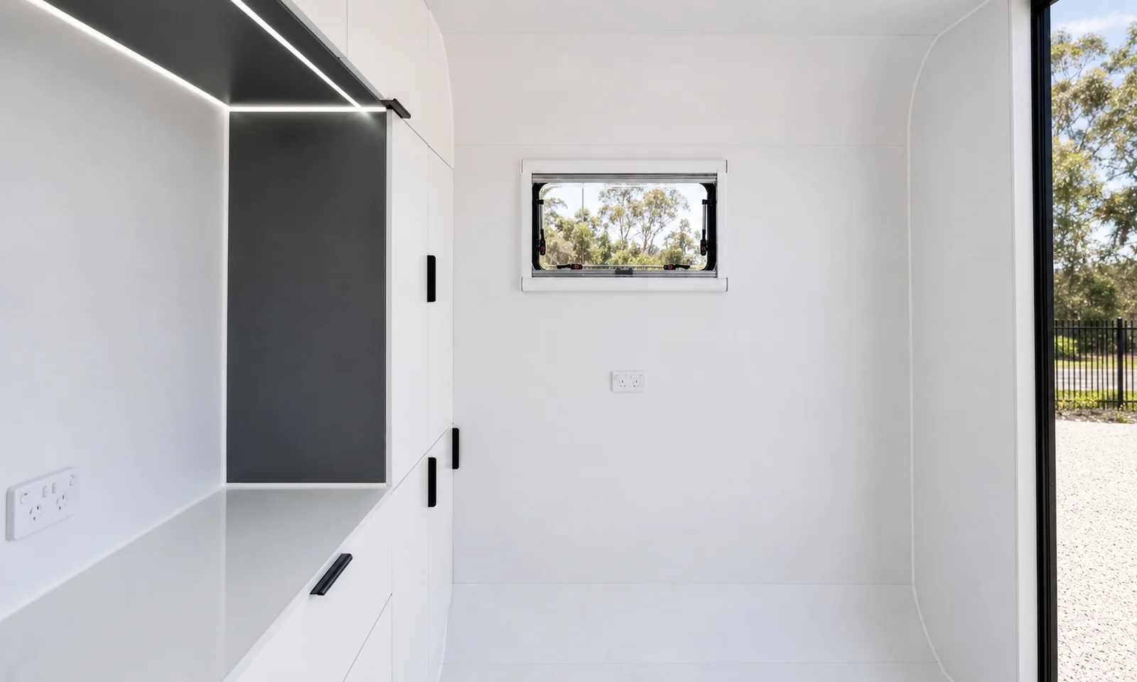 Inside the studio pod, a white bench desk running along the wall under a black shelf with strip lighting, and an awning window above