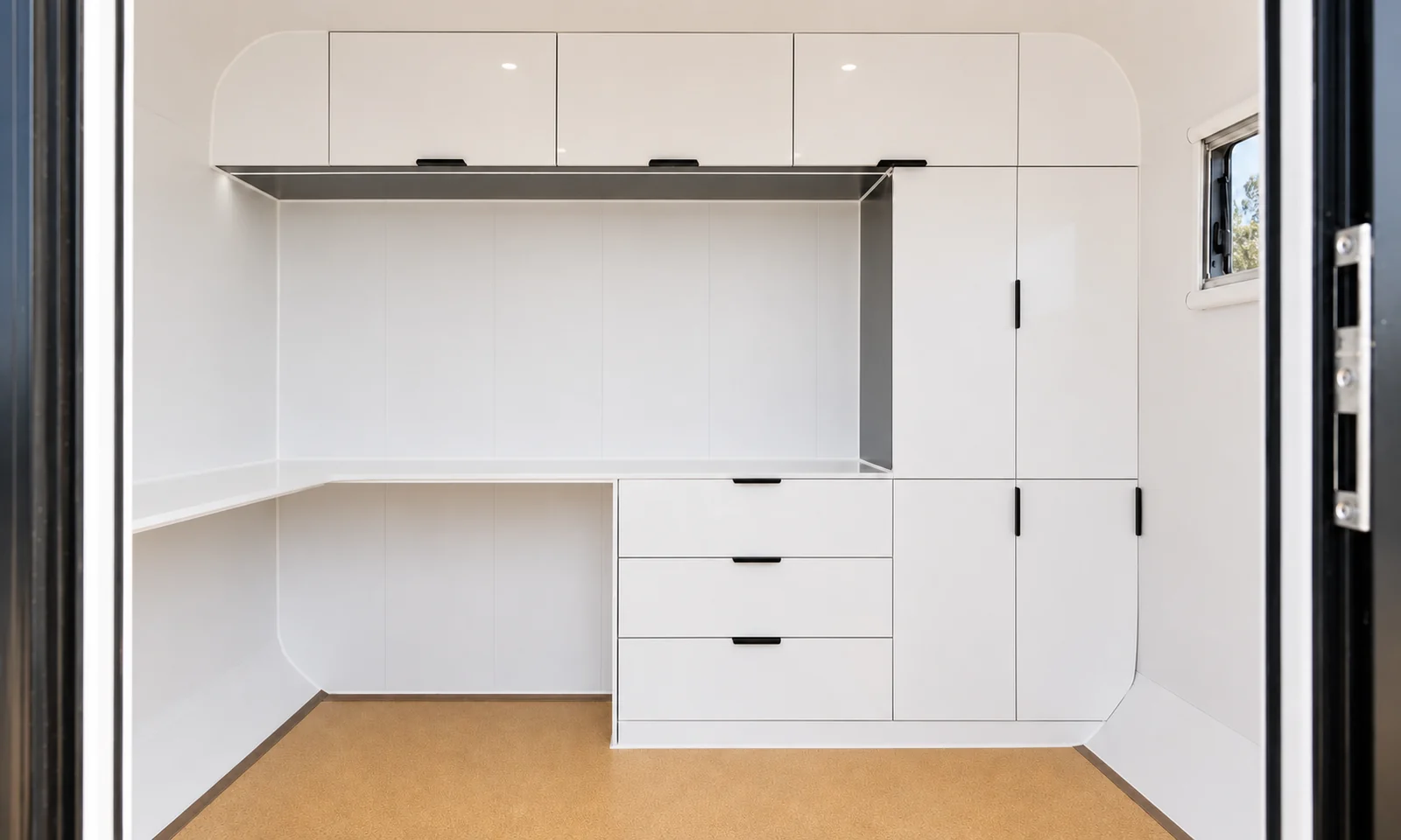 Fitted joinery inside the pod, gloss white overhead cupboards above a desk return with three drawers and a tall cupboard