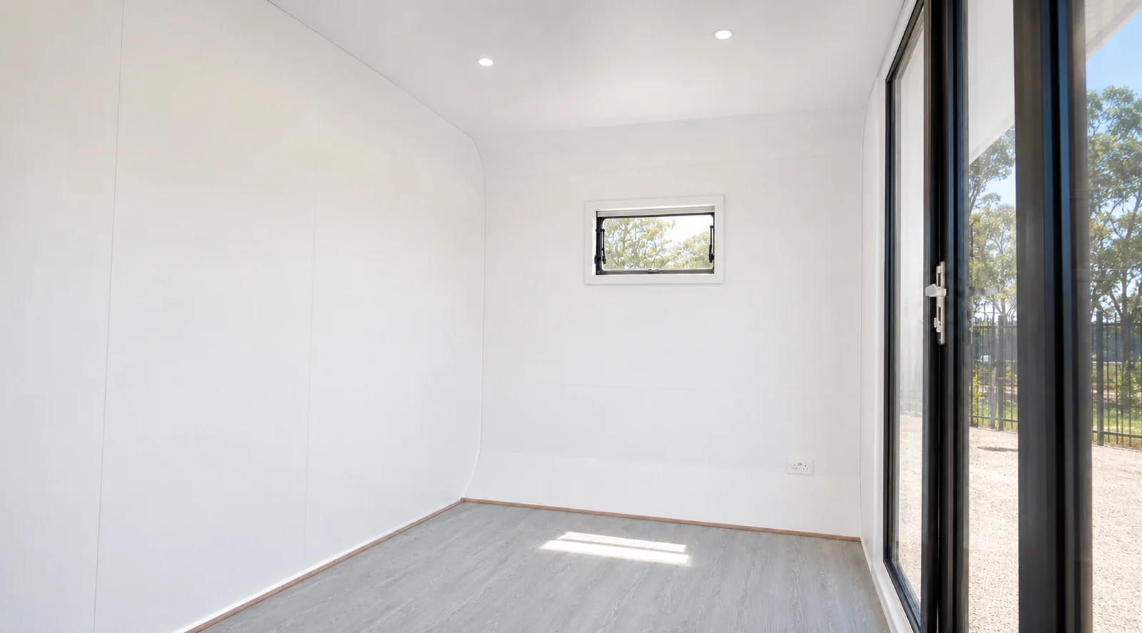 Inside the empty 4 m pod, white lined walls with a small awning window, grey vinyl floor and the glazed door on the right