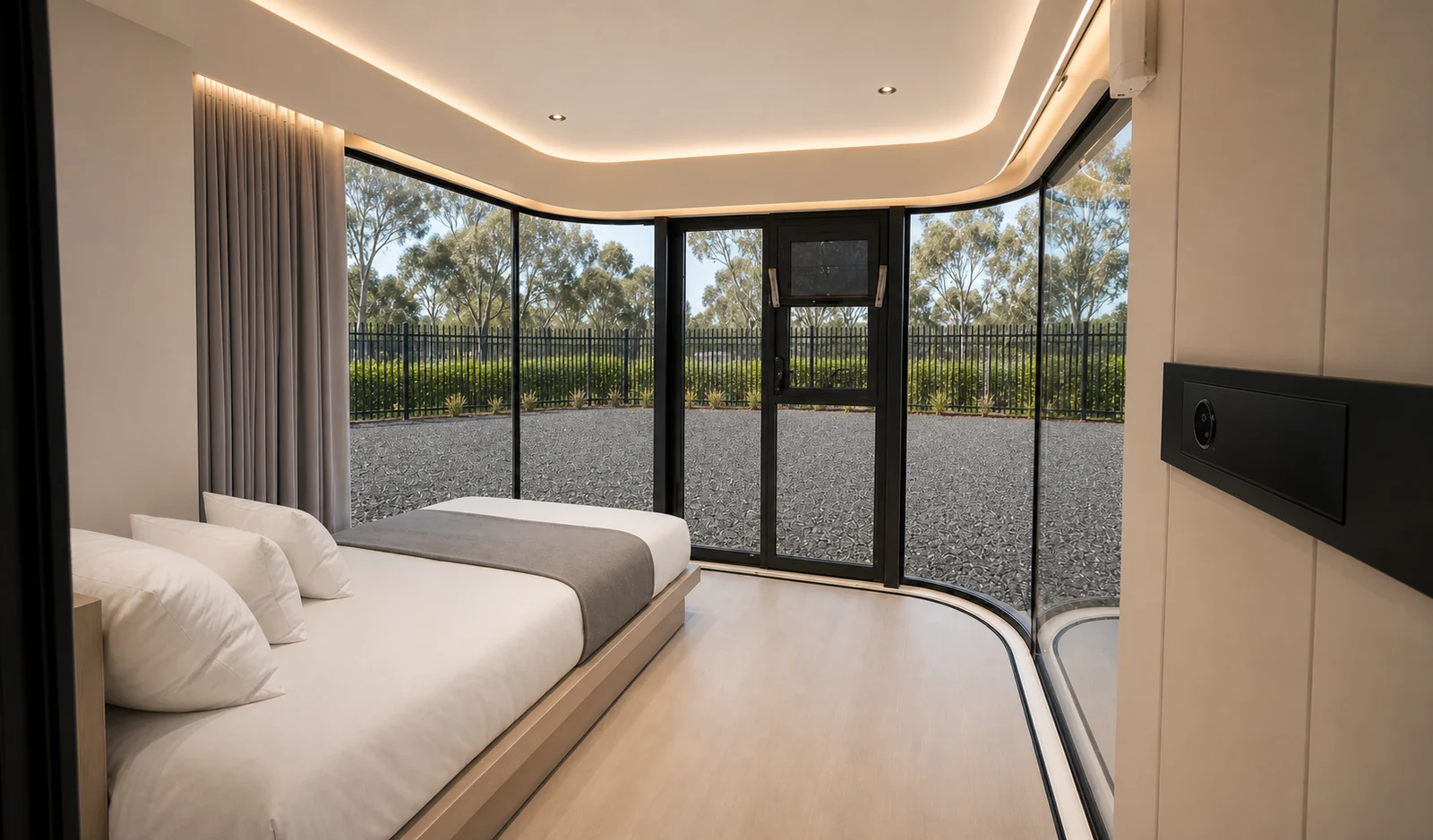 Inside the glass capsule, a low platform bed against the curved wall with concealed cove lighting and glazing wrapping the far corner