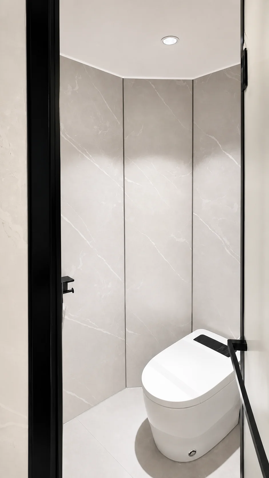 Toilet in the glass capsule set in a stone look alcove with a black framed glass door beside it