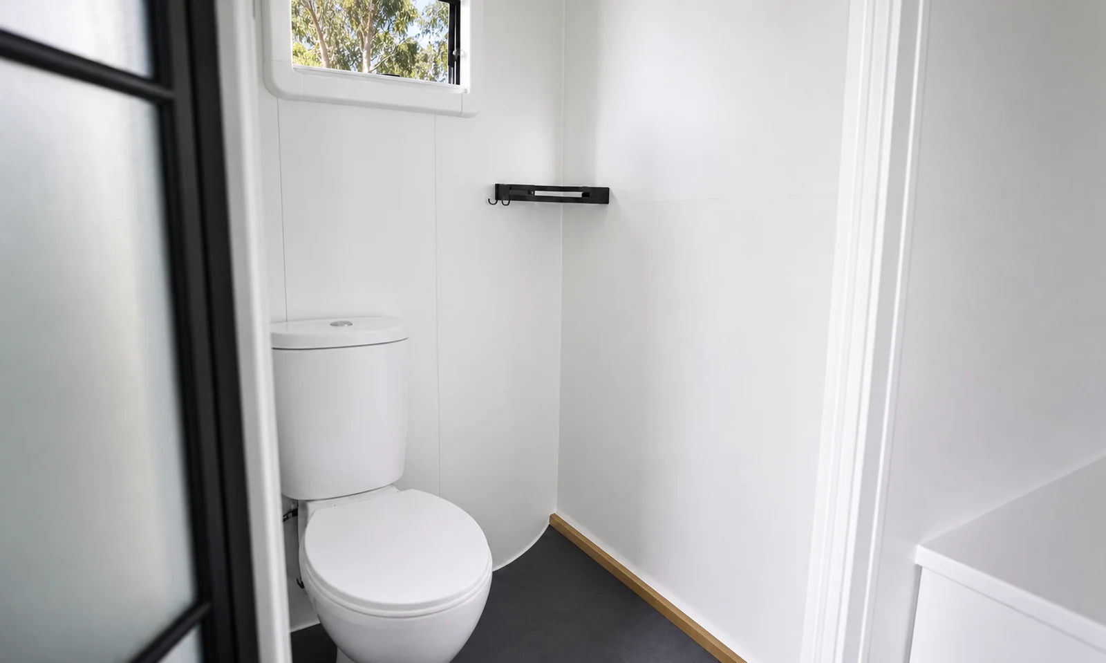 Bathroom in the studio cabin, close coupled toilet against a white wall with a small window above and a shower base to the right