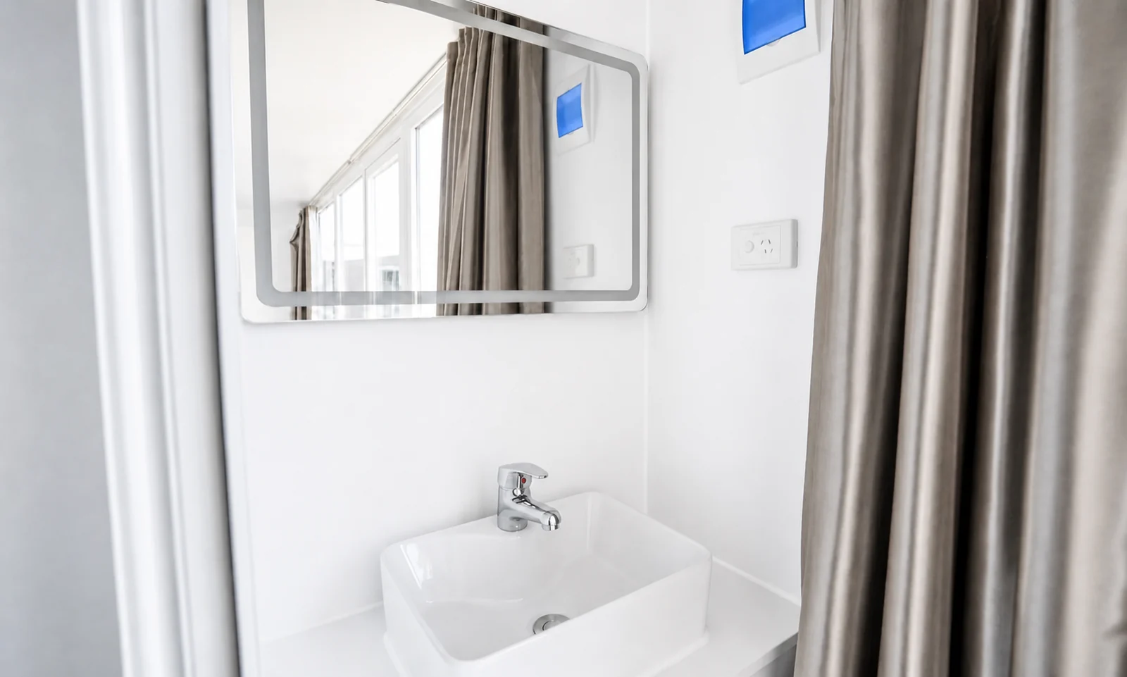Vanity in the studio cabin, rectangular basin with a chrome mixer under a framed mirror, with a shower curtain drawn to one side