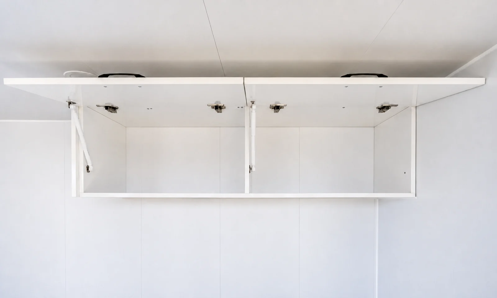 Overhead kitchen cupboards in the studio cabin with the doors open on lift up hinges, showing the empty shelves inside