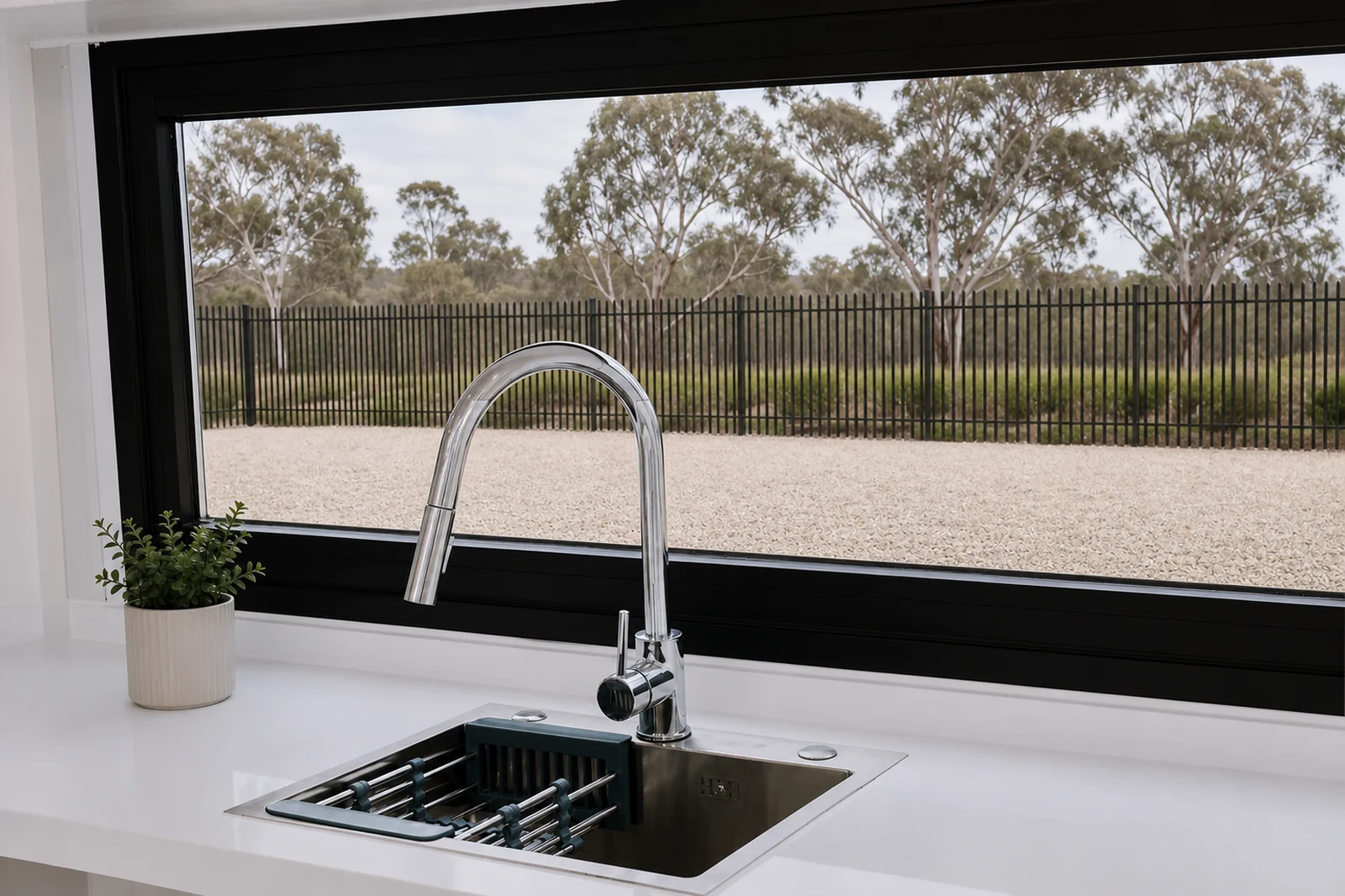 Kitchen sink in the designer pod, stainless undermount sink with a pull down chrome mixer on a white bench under a wide window