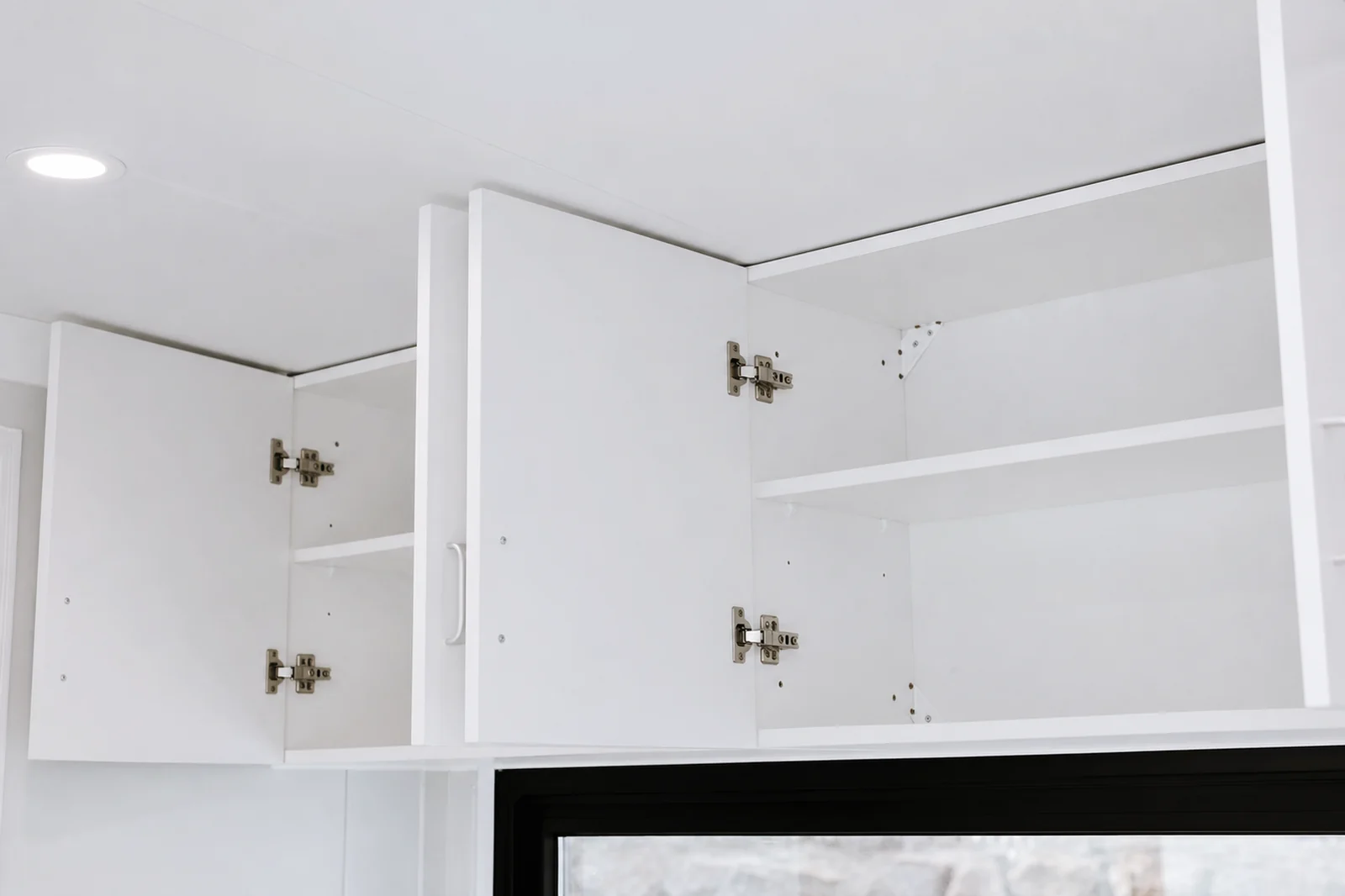 Overhead kitchen cupboards in the designer pod with the doors open showing empty shelves and soft close hinges