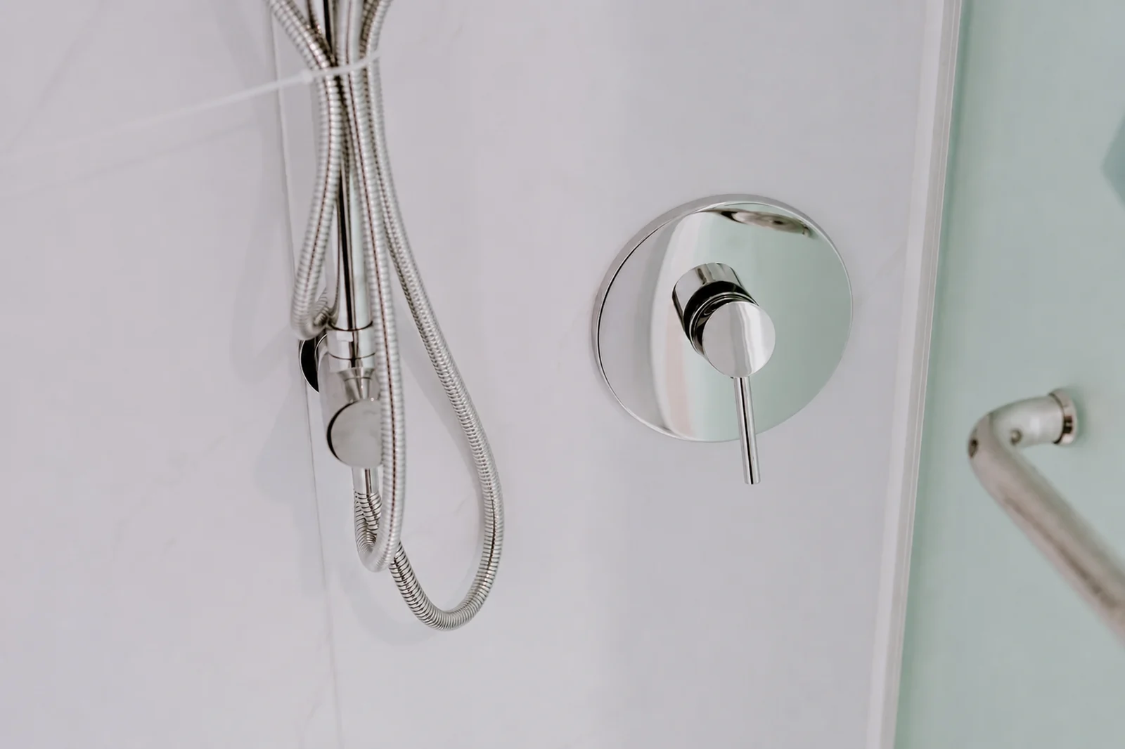 Shower fittings in the designer pod, chrome hand shower on a hook with a mixer and a grab rail on the wall