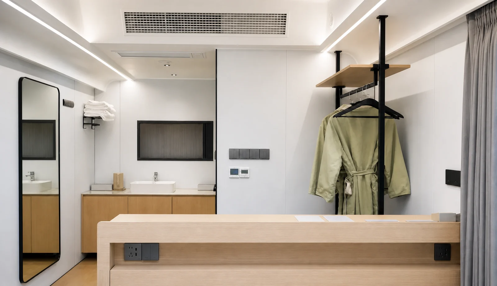Inside the 9.5 m capsule studio, twin timber vanities with basins under a mirror, a full length mirror and a robe on a stand