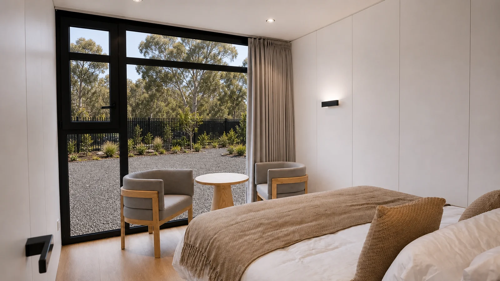 Bedroom in the timber clad capsule, double bed with a caramel throw beside two armchairs and a side table at the glazed corner