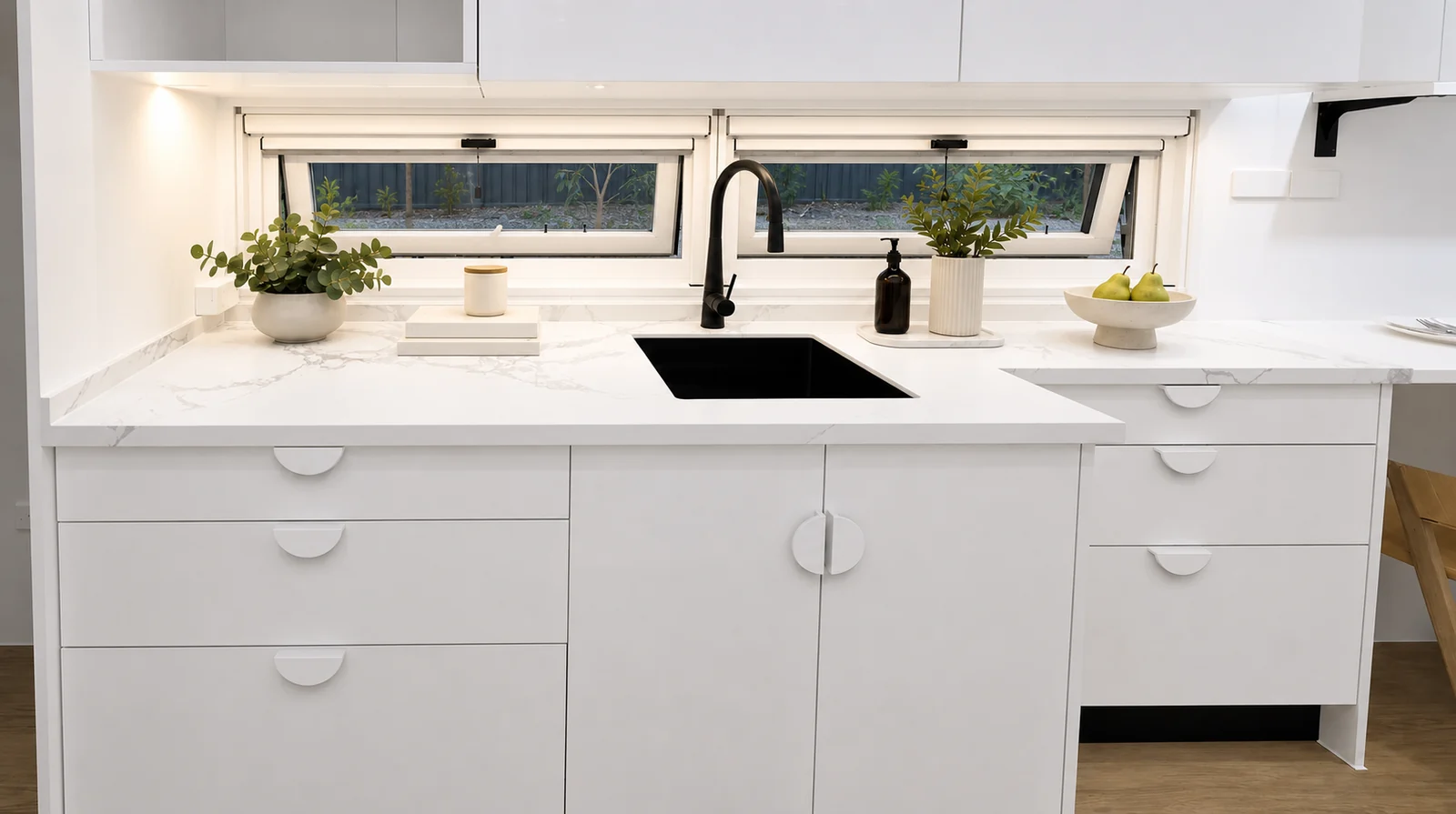 Kitchen island in the veranda tiny home, a pale benchtop with a black undermount sink and mixer below two awning windows