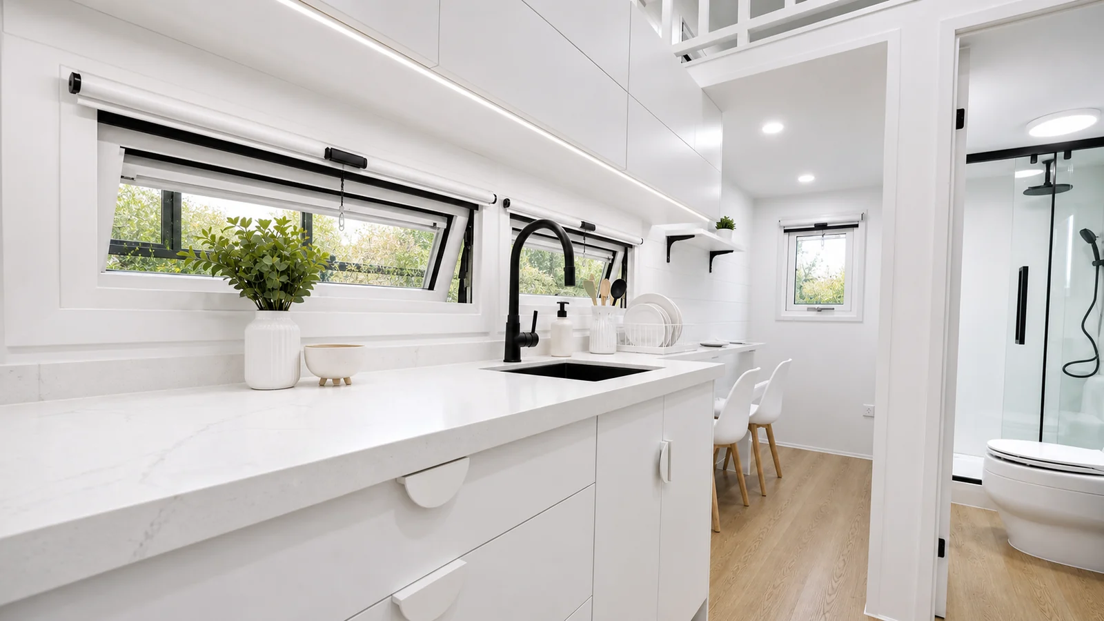 Looking along the kitchen bench of the veranda tiny home to the dining chairs and the bathroom with a shower and toilet at the far end