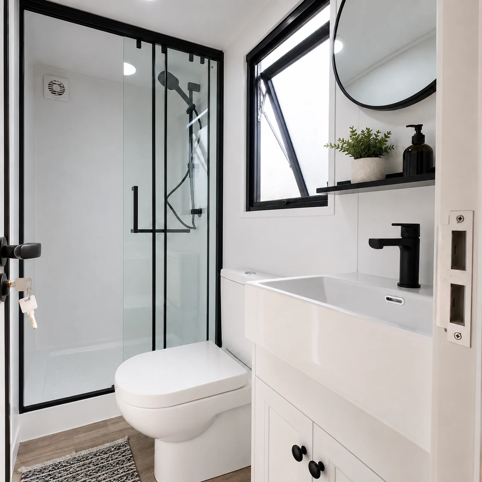 Bathroom in the veranda tiny home, framed glass shower cubicle beside a toilet and a vanity with a round mirror and an awning window