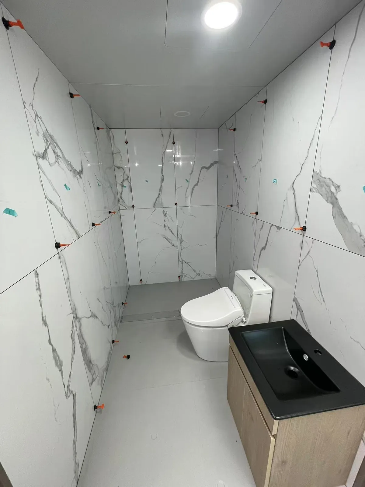 Bathroom pod interior part way through factory fit out, with large format marble look wall panels installed and protective markers still in place