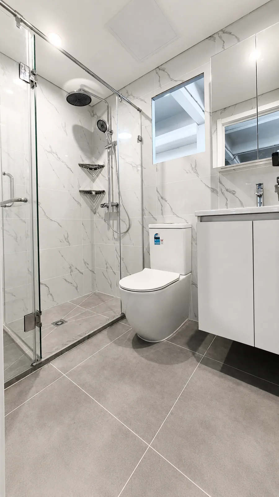 Completed bathroom pod with a hinged glass shower screen, marble look tiling, toilet, vanity and a window