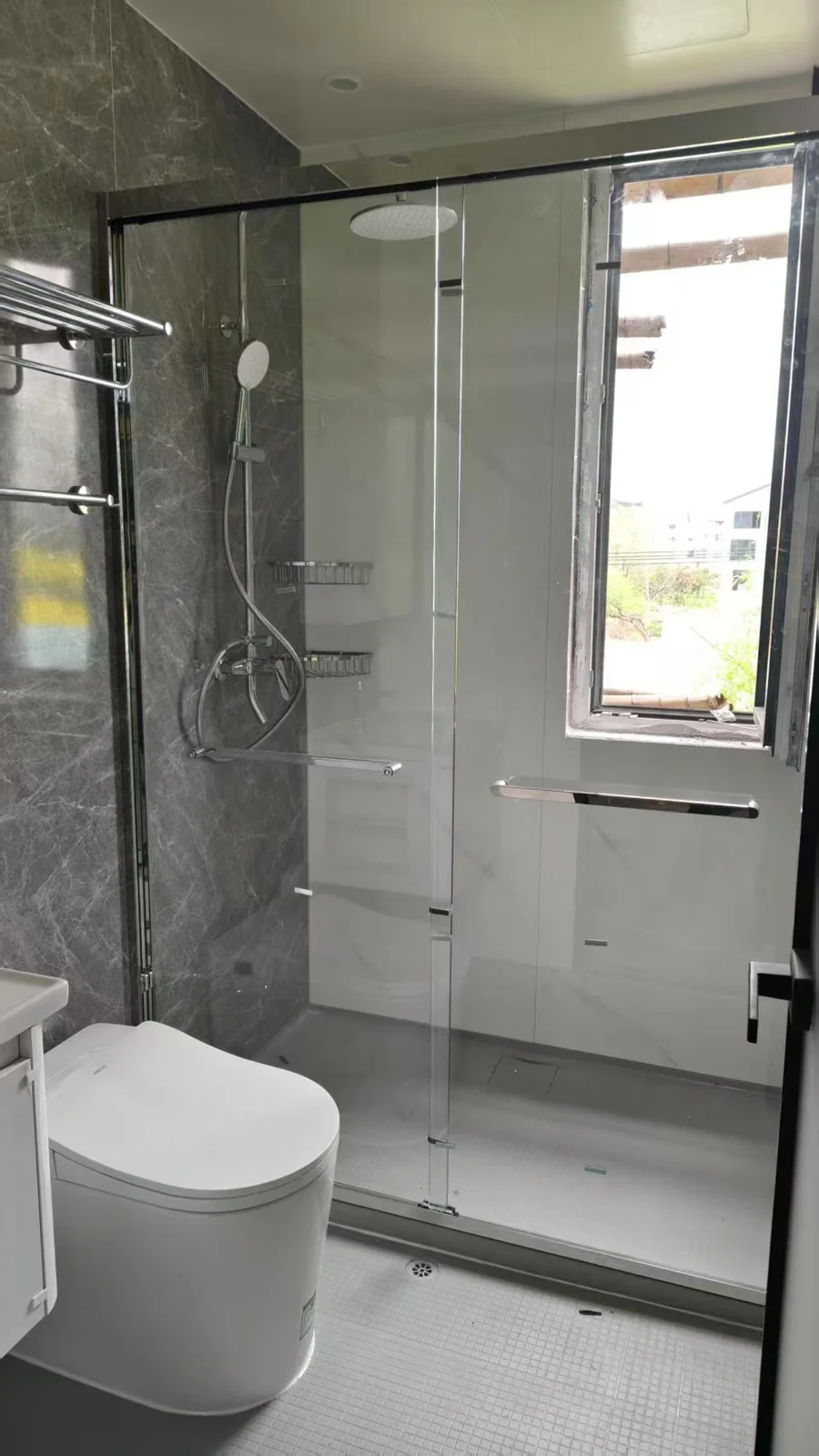 Completed bathroom pod finished in grey marble tiling with a sliding glass shower screen, towel rails and a wall hung toilet